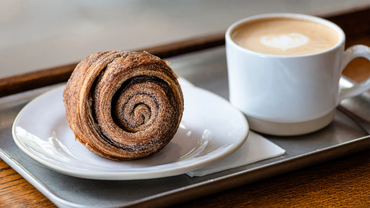 A cinnamon bun and a cup of coffee served for breakfast