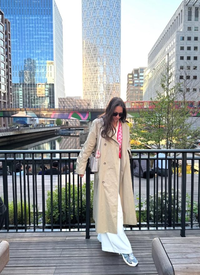 A woman in a cream coat beside the water and city buildings