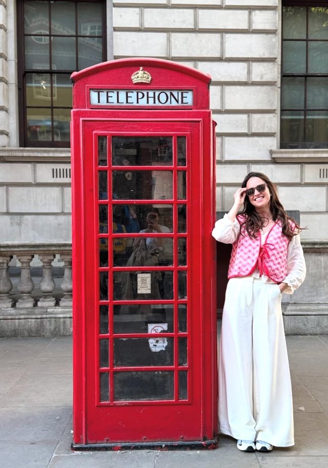A woman smiling beside a red London telephone box